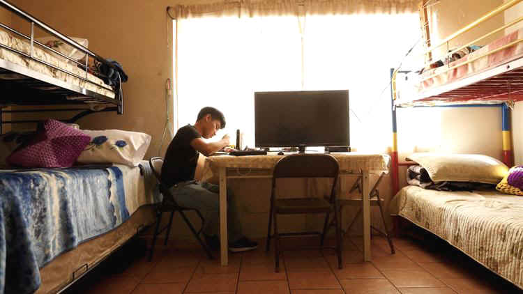 Noe Martinon, 18, does his homework between two sets of bunk beds in a space that is both bedroom a